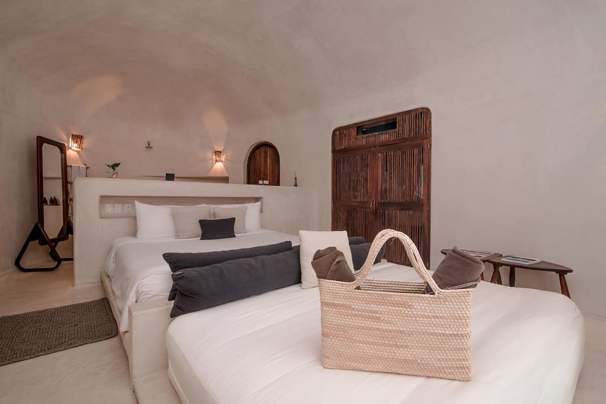 Quarto com duas camas, cabeceira de madeira, cesta de palha e uma pequena mesa com um livro.