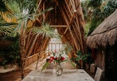 A rustic thatched-roof structure with a wooden table and a vase of flowers in the center.