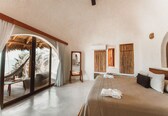 A bedroom with a large bed, a wooden headboard, a mirror, and a view of palm trees through a glass door.