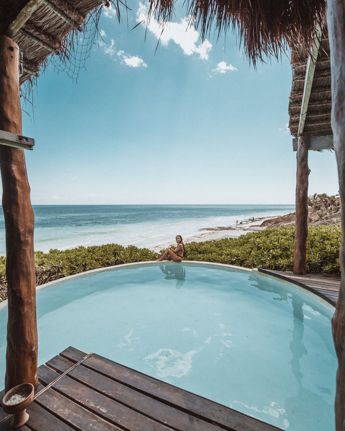 woman sitting on the edge of the pool with the tulum beach on the background