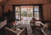 A cozy room with a sloped ceiling, a large window with curtains, a sofa, a table with a vase, and a potted plant.