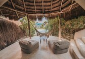 A hammock chair under a thatched roof, two cushioned seating areas, and a view of the ocean.