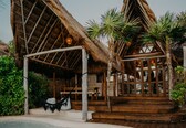 A resort with thatched-roof structures, a pool, and palm trees.