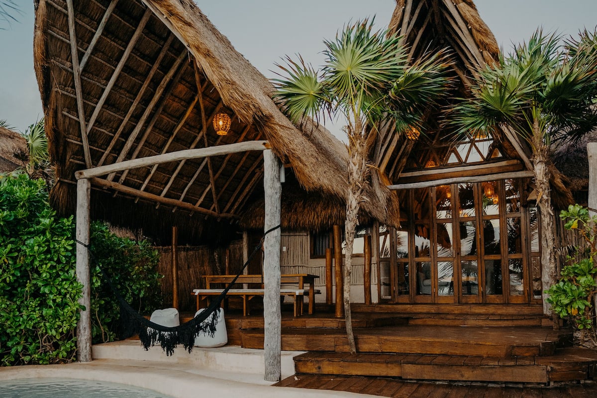 Resort com construções de palha, piscina e palmeiras.