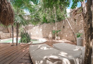 A wooden deck with a hot tub, lounge chairs, and a stone wall.