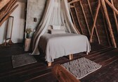 A cozy bedroom with a thatched roof, a canopy bed, and a rustic wooden floor.