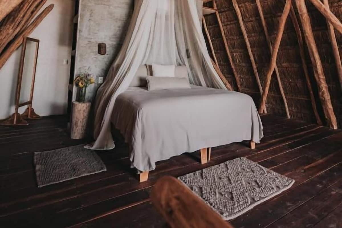 Um quarto aconchegante com telhado de palha, cama com dossel e piso de madeira rústica.