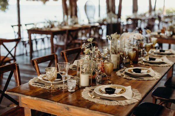 A long wooden table set with glassware, candles, and decorative flowers.