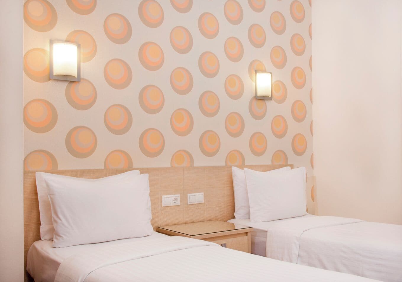 A hotel room with two beds, a wooden headboard, and a patterned wall.