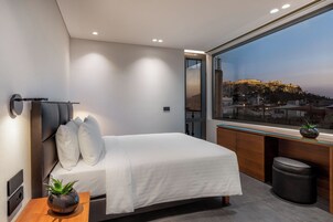 Quarto moderno com cama, mesa de cabeceira e uma janela grande com vista para a cidade.