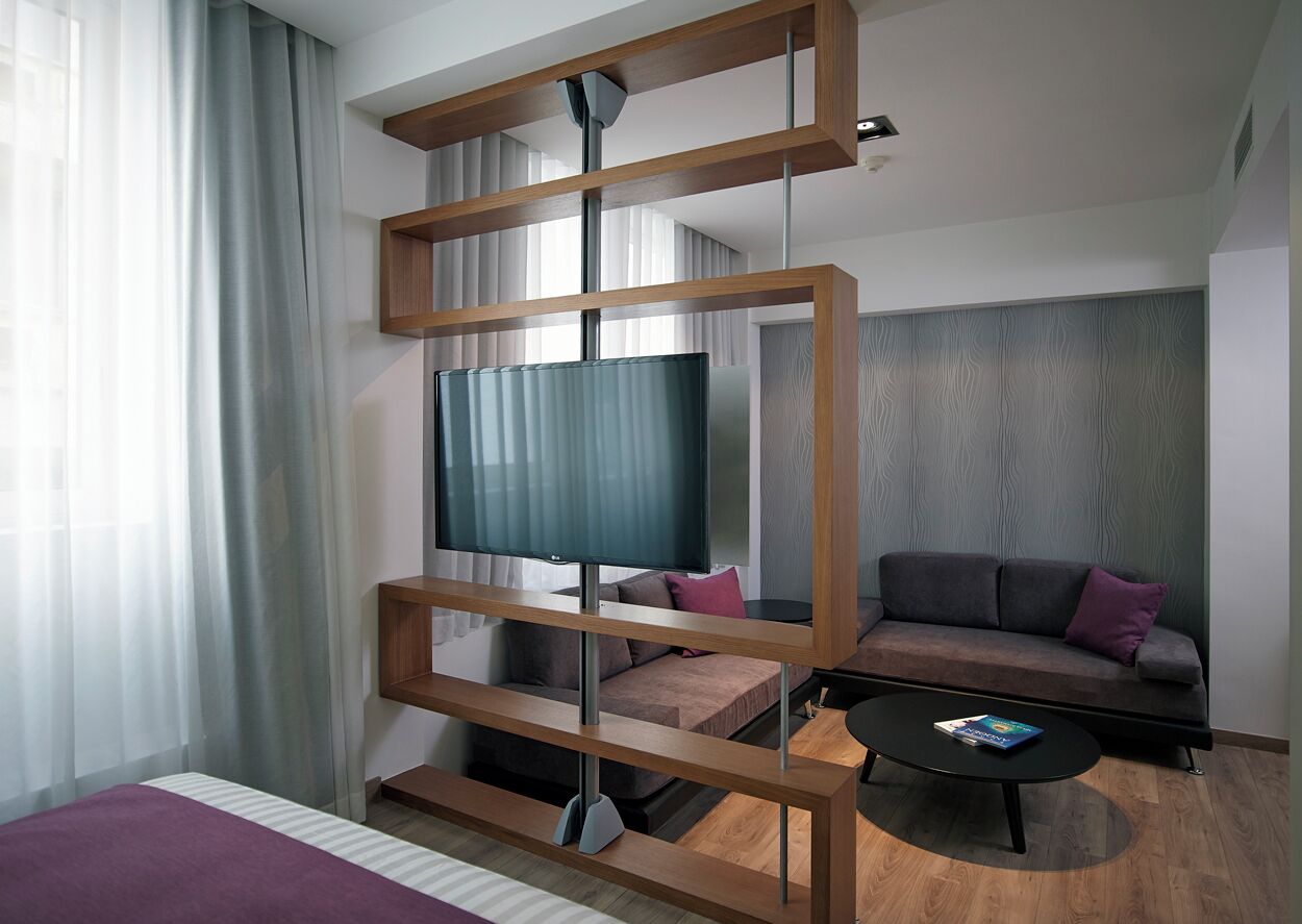 Una habitación de hotel moderna con una cama grande, un televisor montado en un marco de madera, un sofá y una mesa de centro.