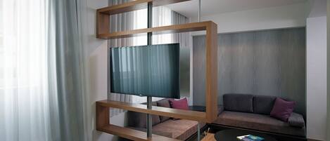 Una habitación de hotel moderna con una cama grande, un televisor montado en un marco de madera, un sofá y una mesa de centro.