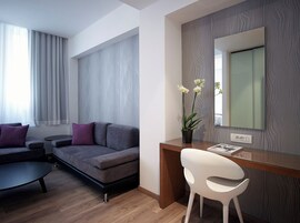 Quarto moderno com sofá cinzento, cadeira branca, escrivaninha de madeira e um espelho grande.