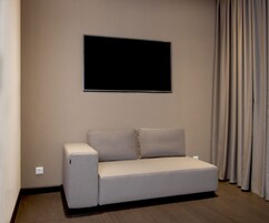 Uma sala de estar moderna com uma televisão de tela plana na parede, um sofá claro e uma cortina à direita.
