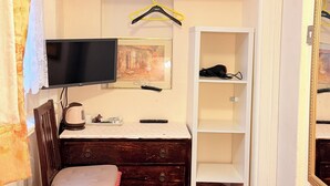 A compact room with a bed, a desk with a TV, a chair, a wardrobe, and a shelf with a mirror.