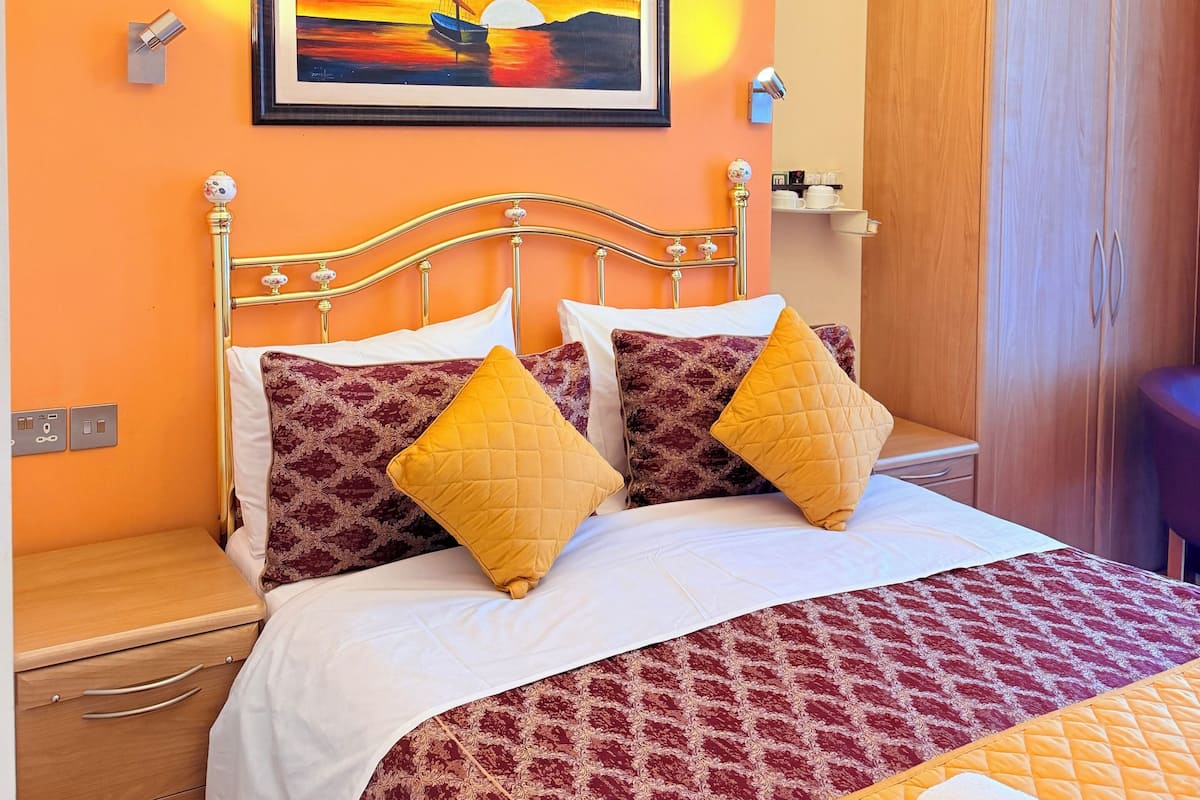 A bed with a headboard, two pillows, a bedside table, a nightstand, a wardrobe, a painting, and a chandelier.