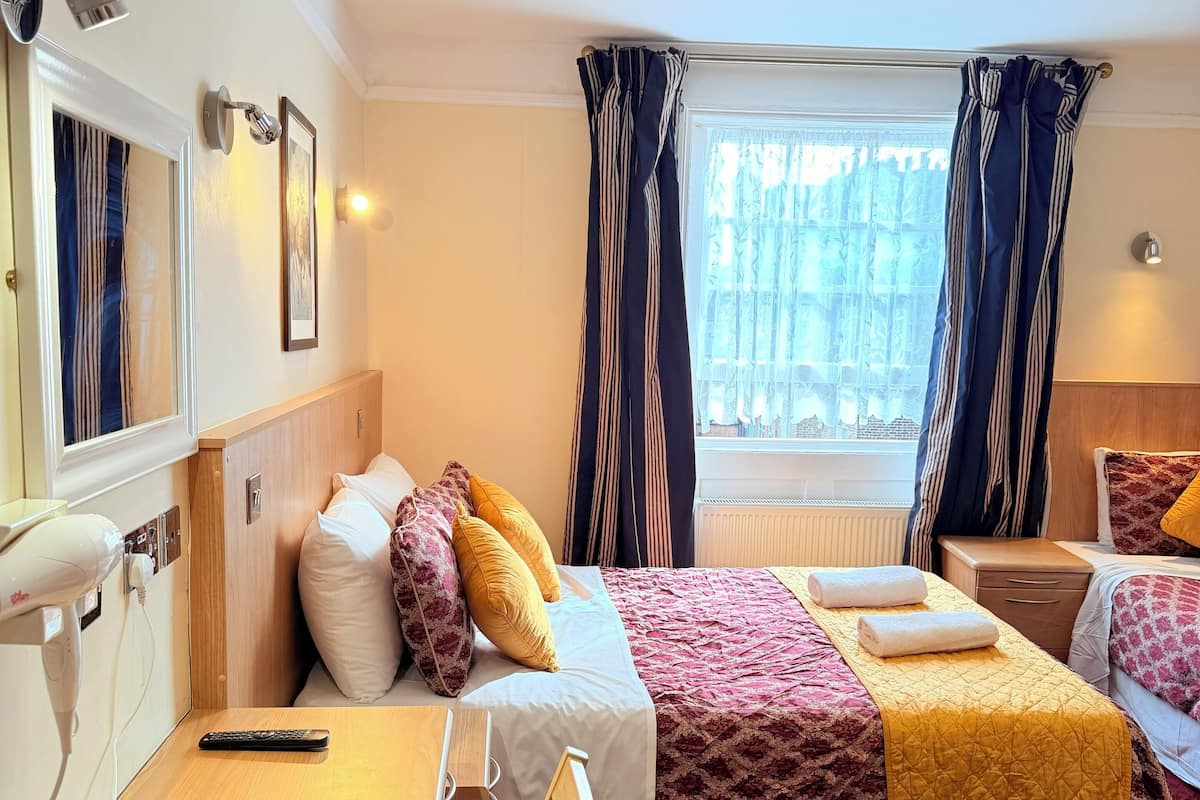 A hotel room with two beds, a desk, a chair, a hairdryer, a mirror, and a window with curtains.