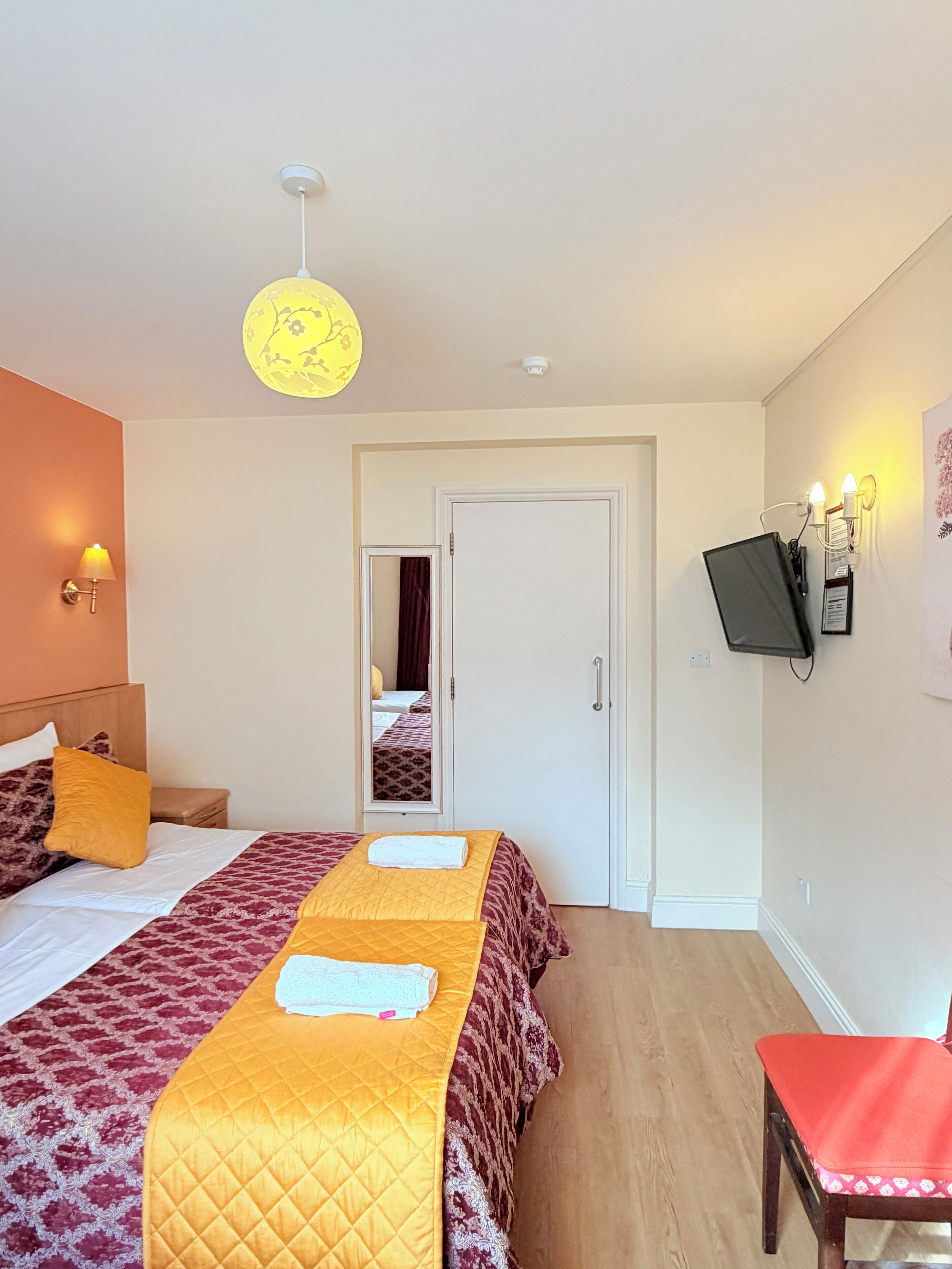 A hotel room with a bed, a red chair, a TV mounted on the wall, and a door leading to another room.
