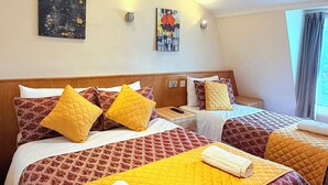 A hotel room with two beds, each with a quilted bedspread, multiple pillows, and a painting on the wall.