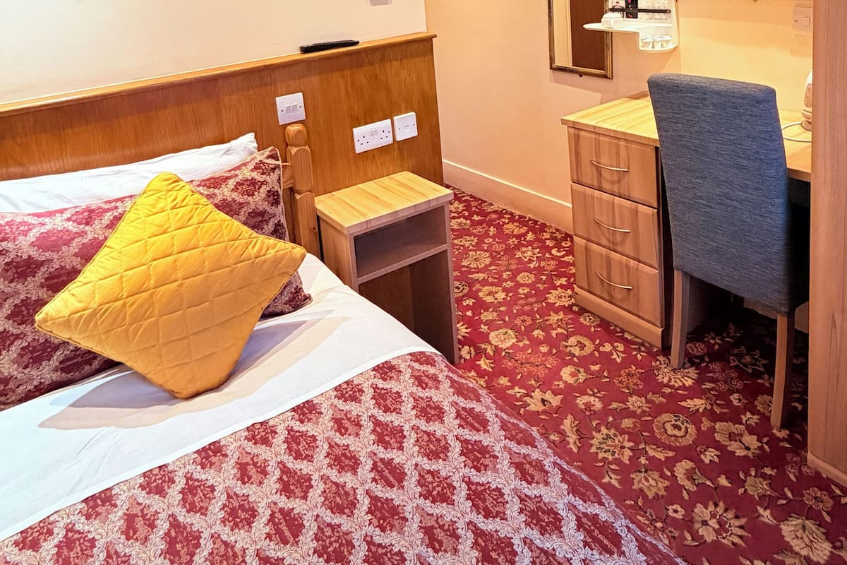 A hotel room with a bed, bedside table, mirror, desk, chair, and carpeted floor.