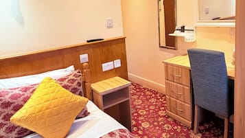 A hotel room with a bed, bedside table, mirror, desk, chair, and carpeted floor.