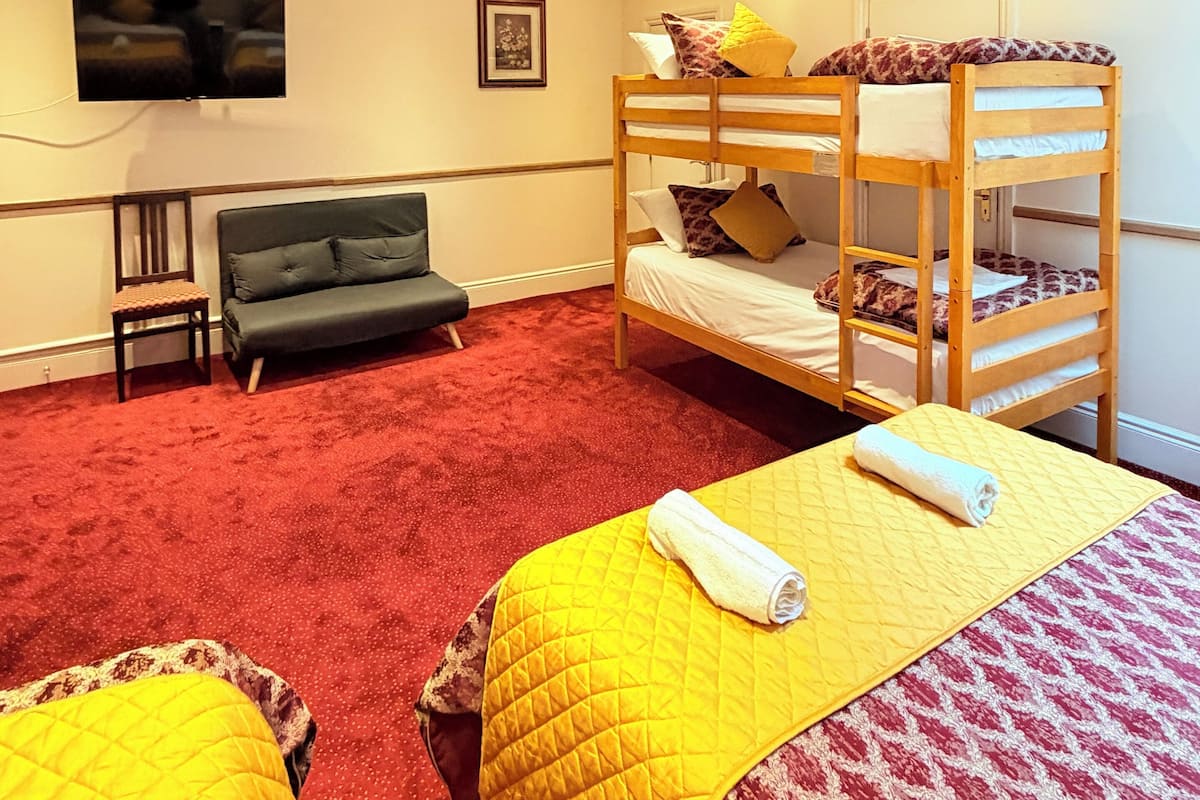 A room with bunk beds, a sofa, a TV, and a red carpet.