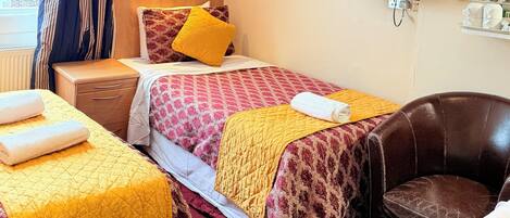 A hotel room with two beds, a TV, a chair, and a window with curtains.
