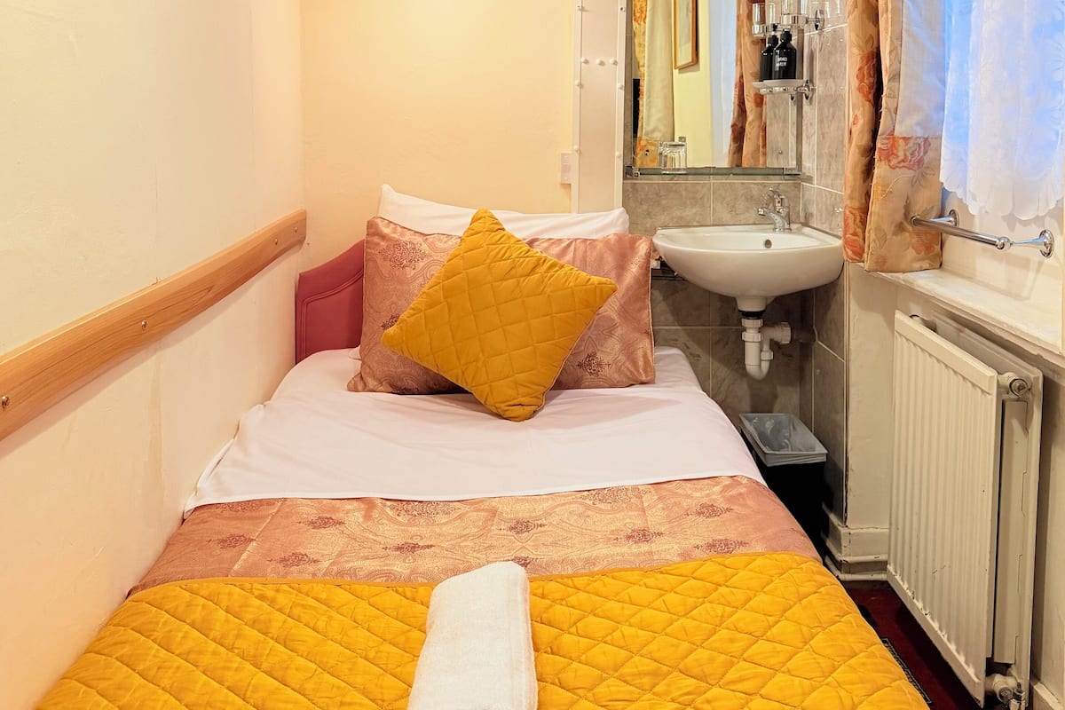 A hotel room with a bed, a bedside table, a mirror, a sink, and a window with curtains.