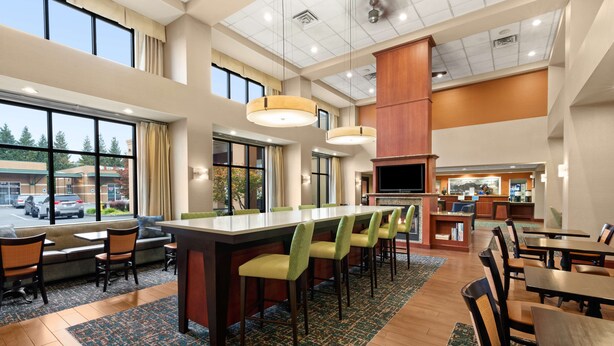 A spacious hotel lobby with a long reception desk, multiple seating areas, and a large window offering a view of the parking lot.