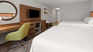 A hotel room with a wooden desk, a green chair, a flat-screen TV, a bed, and a door.