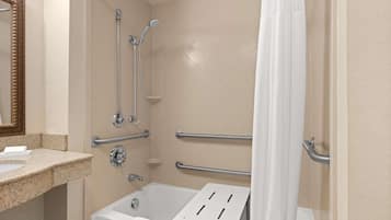 A bathroom with a bathtub, a shower with grab bars, a sink, and a mirror.