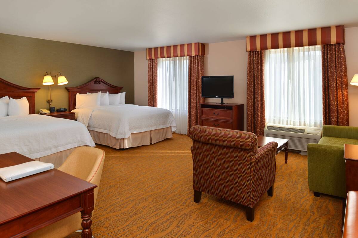 A hotel room with two beds, a television, a desk, and a chair.