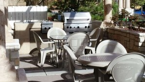 Eine Terrassenanlage im Freien mit Grill, weißen Stühlen und einem Tisch.