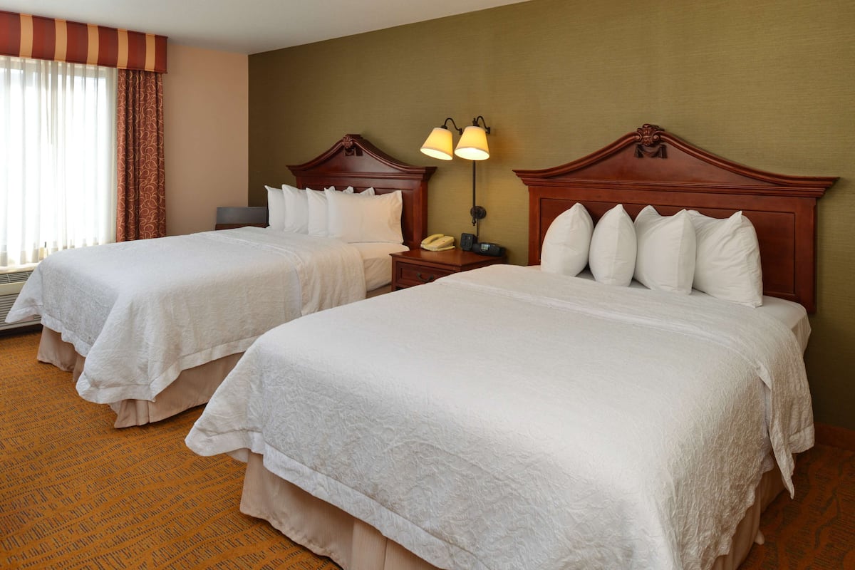 A hotel room with two beds, a nightstand with a lamp, and a window with curtains.