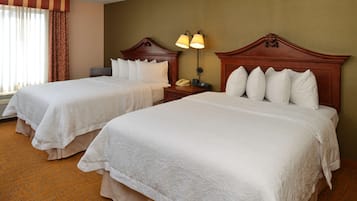 Una habitación de hotel con dos camas, una mesita de noche con lámpara y una ventana con cortinas.