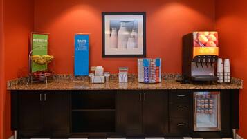 A hotel reception area with a granite countertop, a beverage dispenser, a refrigerator, and a framed picture on the wall.