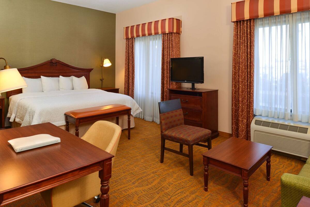 A hotel room with a bed, a desk, a chair, a television, and a window with curtains.