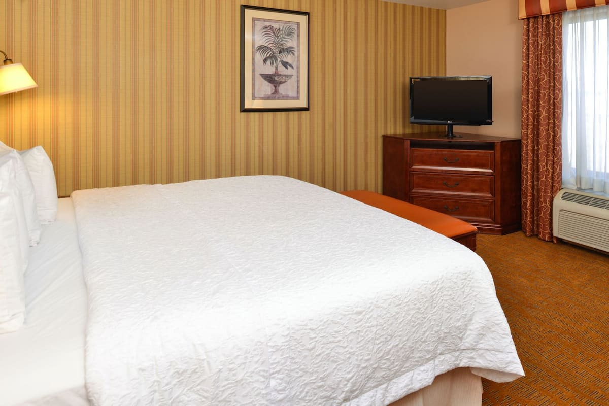 A hotel room with a large bed, a television on a wooden dresser, and a framed picture on the wall.
