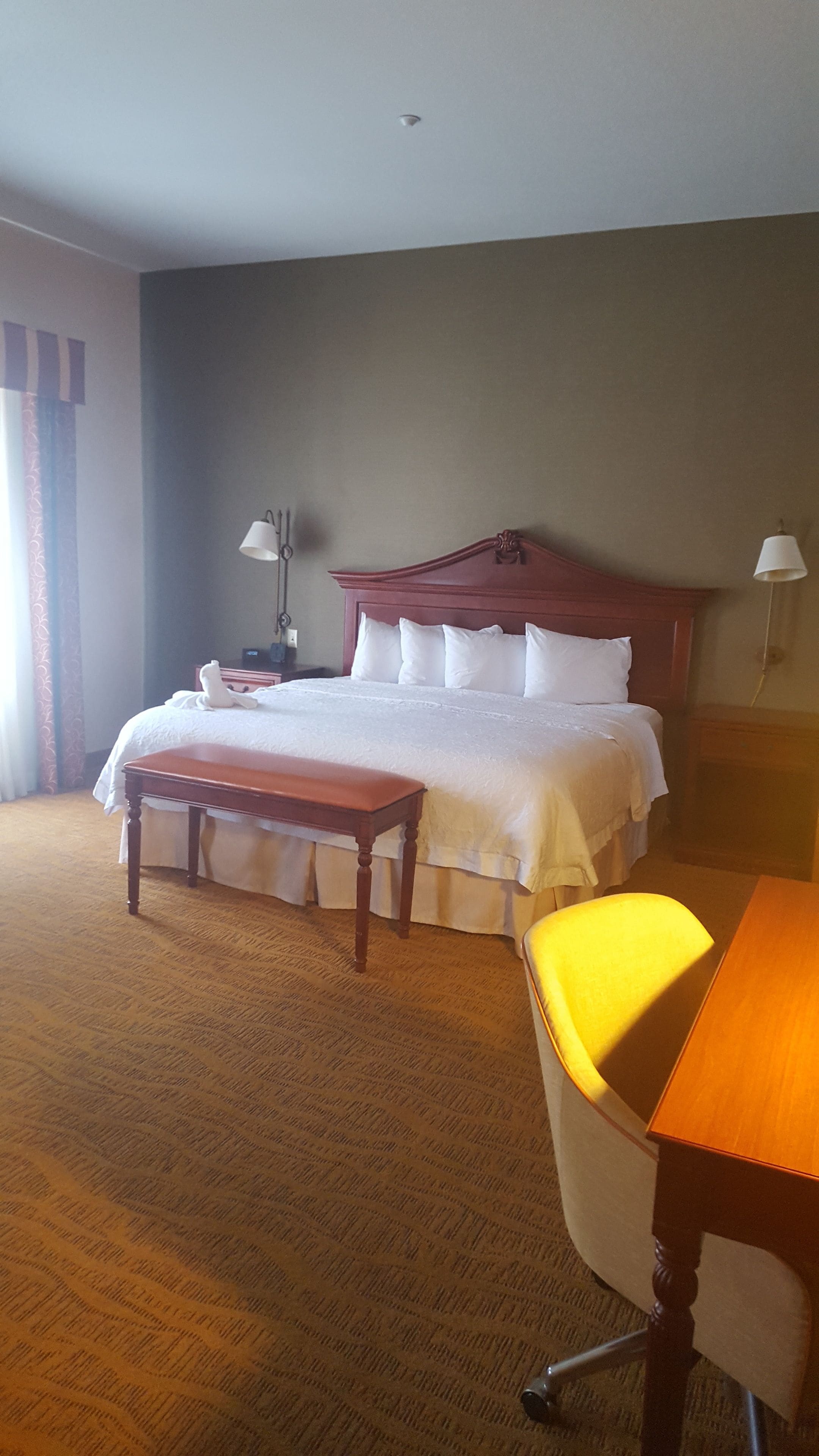 A hotel room with a large bed, a wooden bench, a desk, and two lamps.