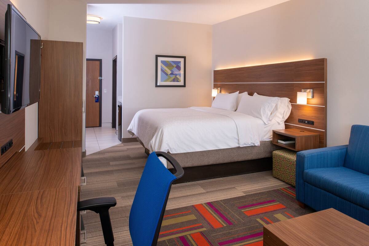 A hotel room with a bed, a desk, a chair, a TV, and a nightstand with a lamp.