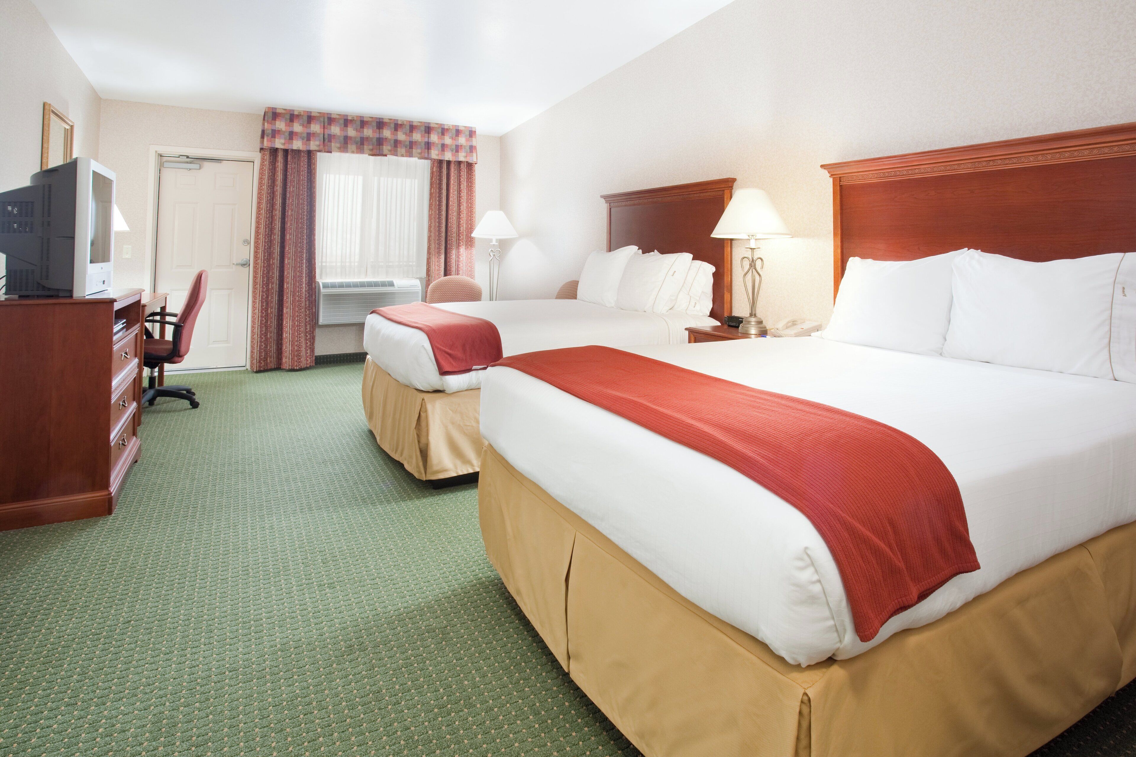 A hotel room with two beds, a desk with a television, a chair, and a window with curtains.