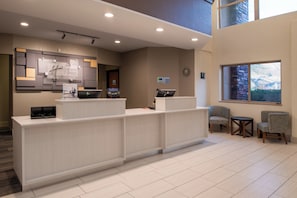 Un espace d’accueil d’hôtel au design moderne, comprenant un comptoir d’accueil, un coin salon et une horloge murale.