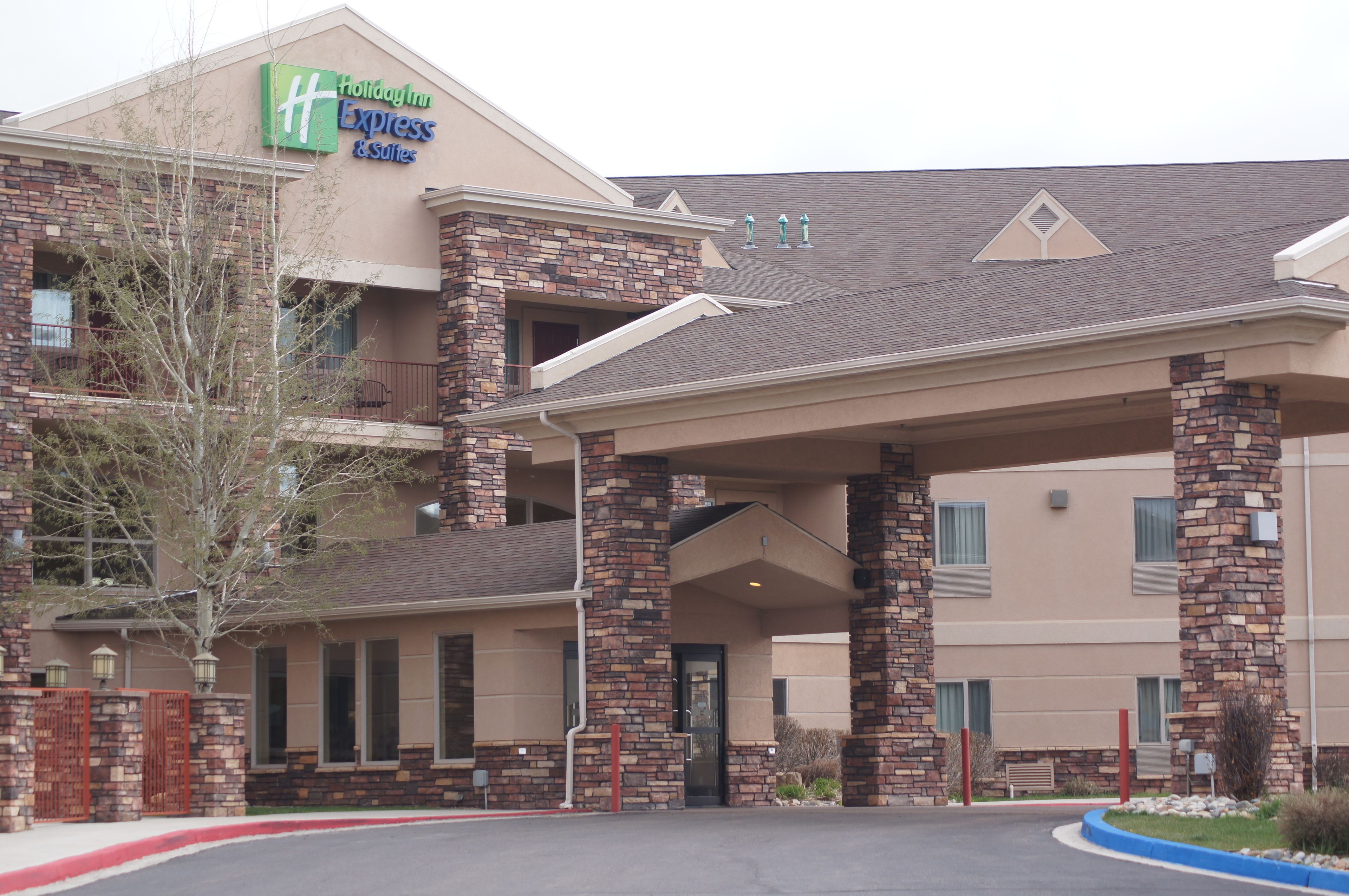 Un bâtiment de l’hôtel Holiday Inn Express & Suites, avec une façade en briques, une entrée abritée et un parterre aménagé devant.
