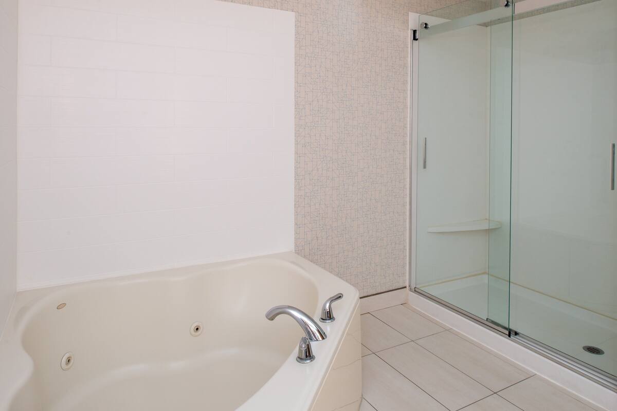 A bathroom with a bathtub, a glass shower enclosure, and tiled flooring.