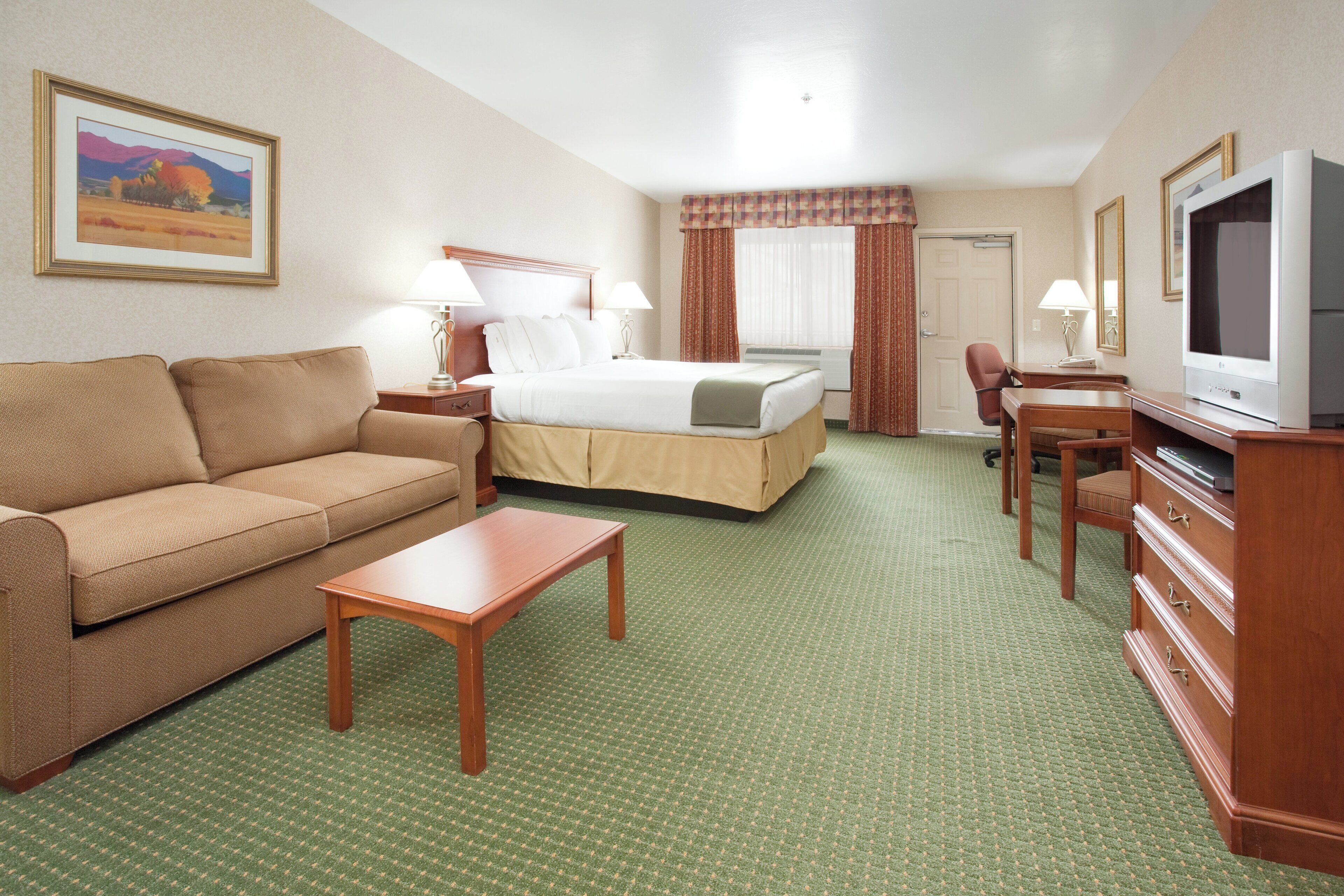 Ein Hotelzimmer mit Bett, einer Couch, einem Fernseher, einem Schreibtisch und Teppichboden.