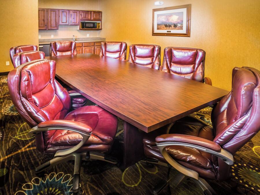 Un salón de conferencias con una amplia mesa de madera rodeada de sillones de cuero, un microondas y un cuadro en la pared.