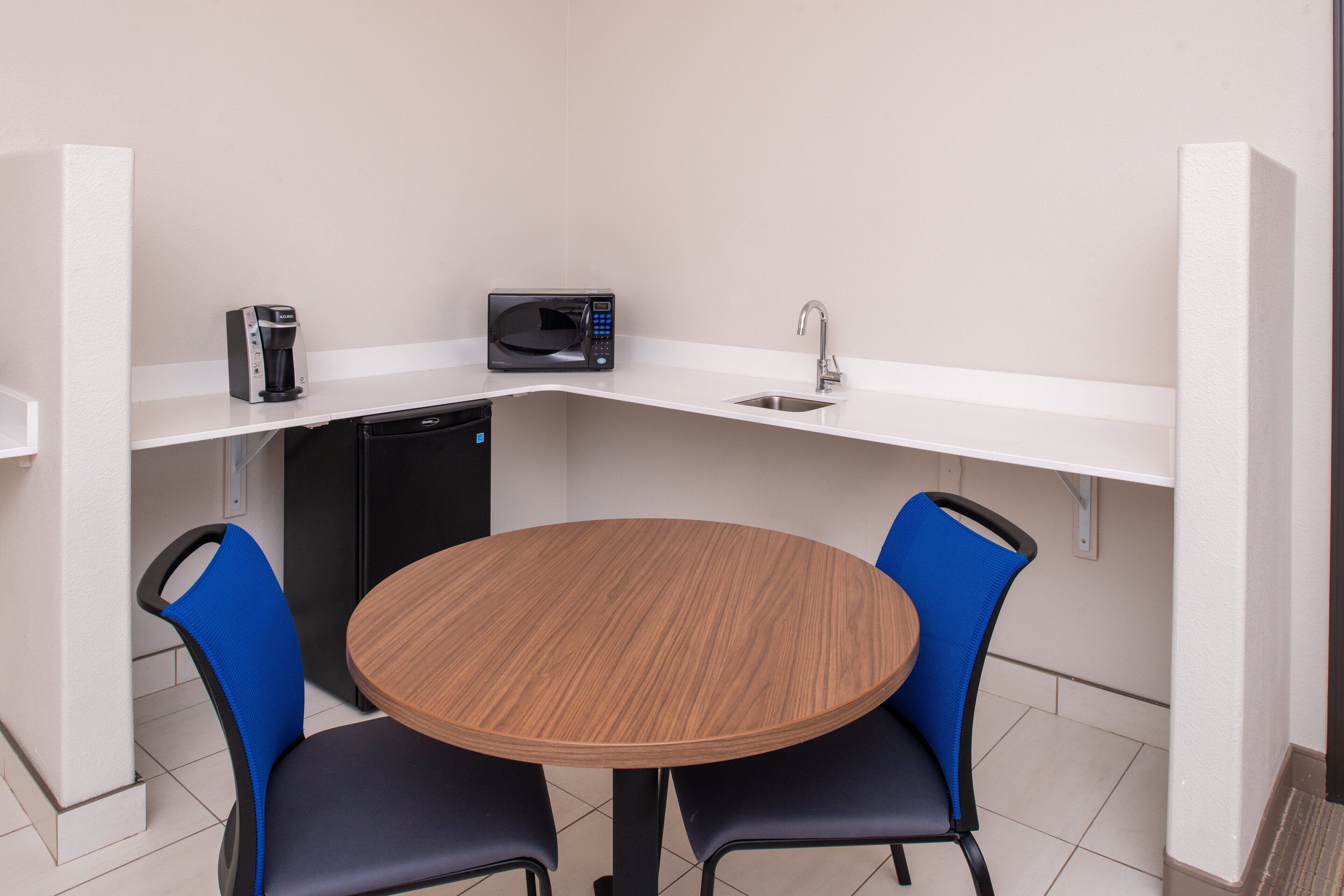 A small kitchenette with a microwave, coffee maker, and sink. There is a round wooden table with two chairs.