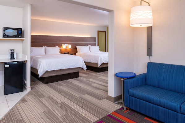 A hotel room with two beds, a microwave, a coffee maker, a blue sofa, and a small table.