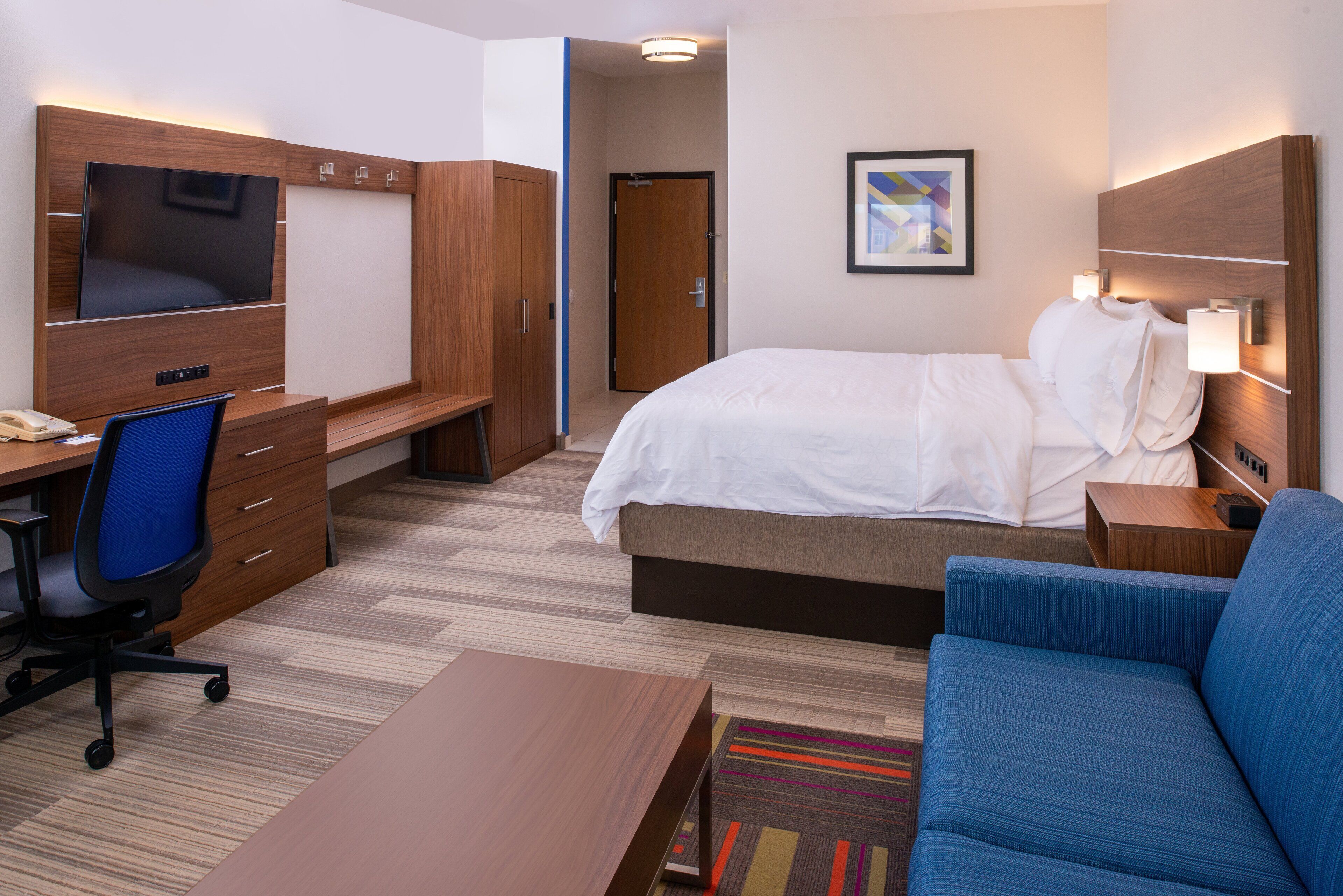 A hotel room with a bed, a desk with a chair, a TV, and a sofa.