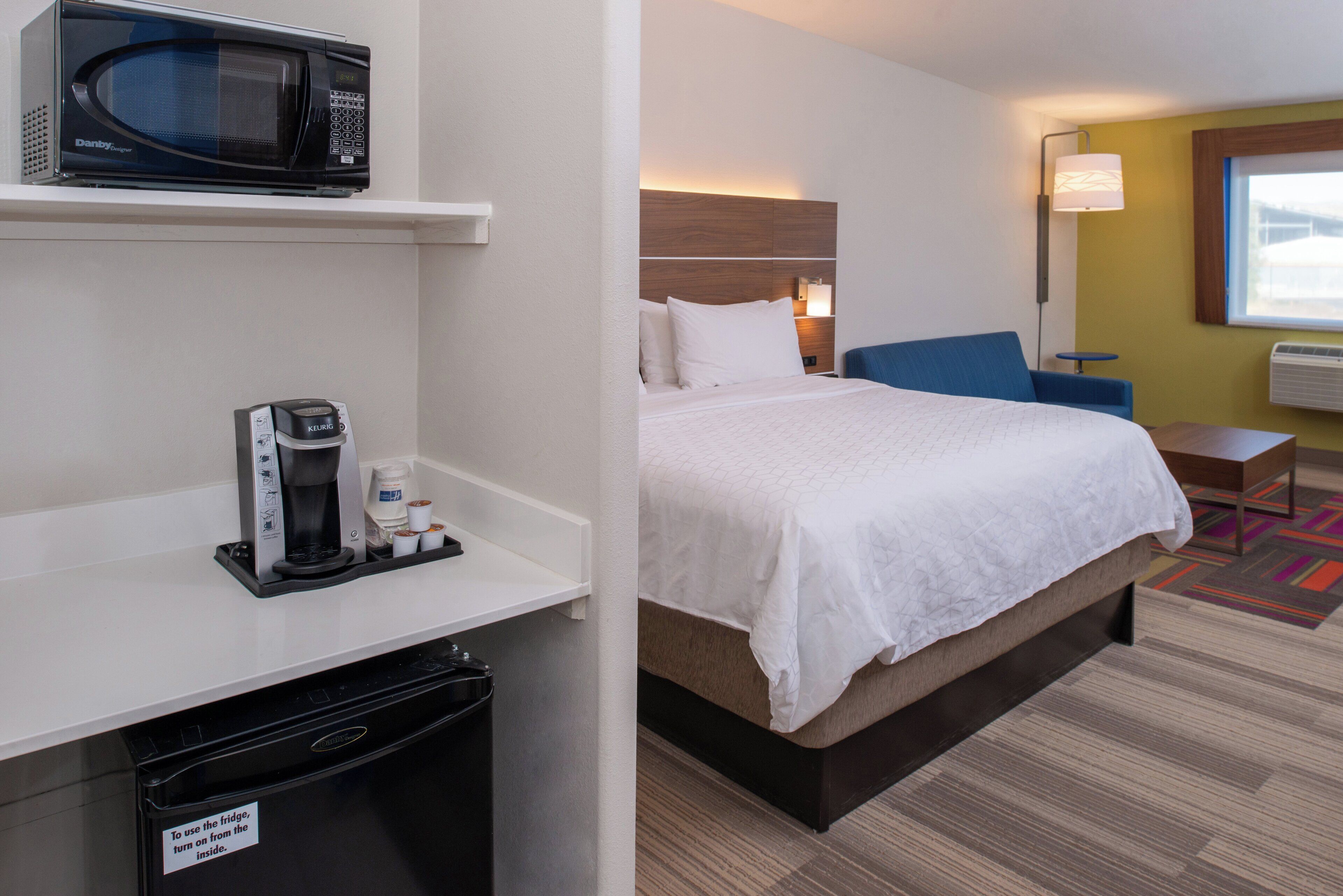 A hotel room with a bed, a coffee maker, a microwave, a desk, and a chair.